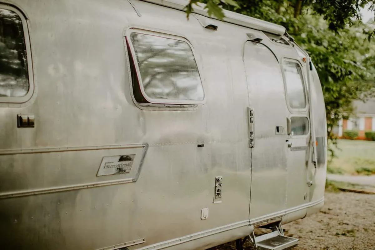 A close-up of the Airstream’s aluminum exterior, showcasing its sleek, modern lines, windows, and the inviting door handle. The image evokes feelings of adventure, independence, and the beginning of a new urban journey.