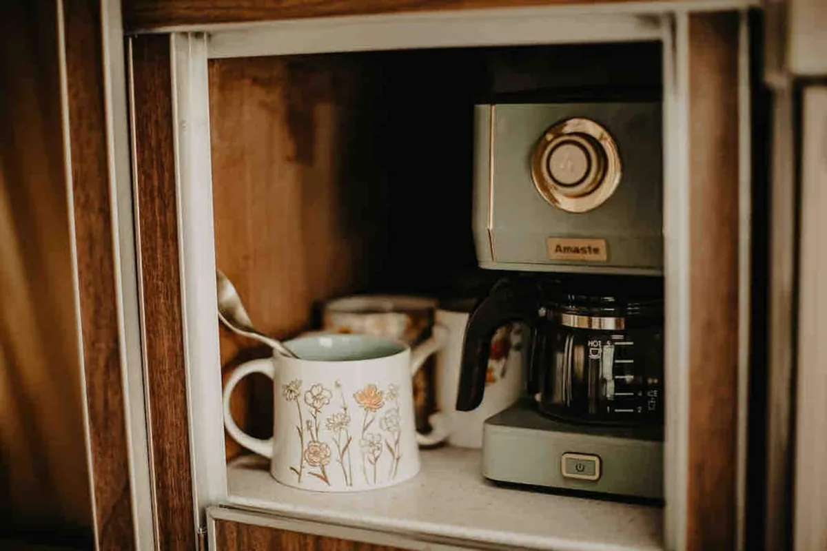 A close-up of a coffee maker with decorative mugs and a spoon, staged on a countertop with soft, inviting lighting. The setup feels intimate and personal, ideal for a romantic coffee date or a leisurely morning routine.