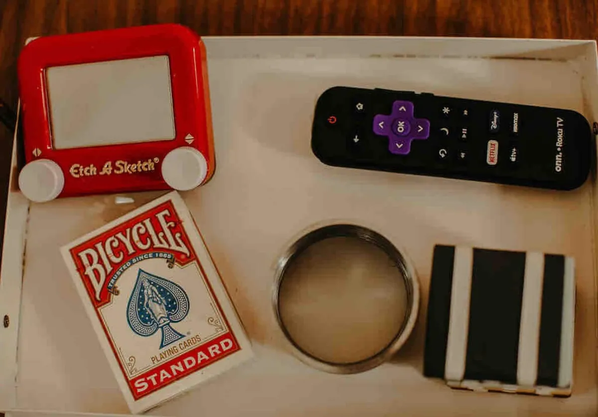 A tabletop collection of whimsical items—an Etch A Sketch, a deck of Bicycle playing cards, a remote, and a striped object—sits ready for spontaneous creativity and fun. The playful grouping nods to vintage nostalgia and encourages guests to unwind, play games, and capture Instagrammable moments.