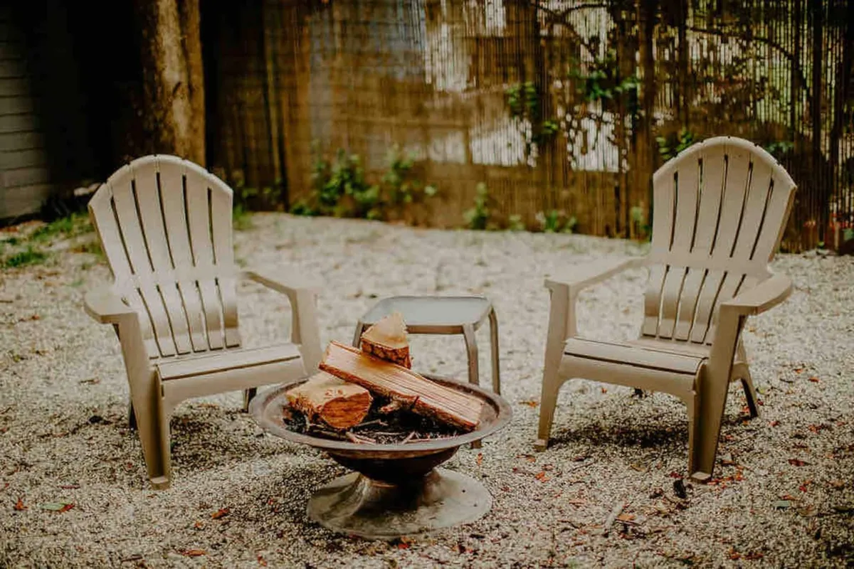 An inviting outdoor campfire area with Adirondack chairs arranged around a fire pit set on gravel. The scene is ready for gatherings, storytelling, and making s’mores, with the outdoors promising memorable evenings under the stars.