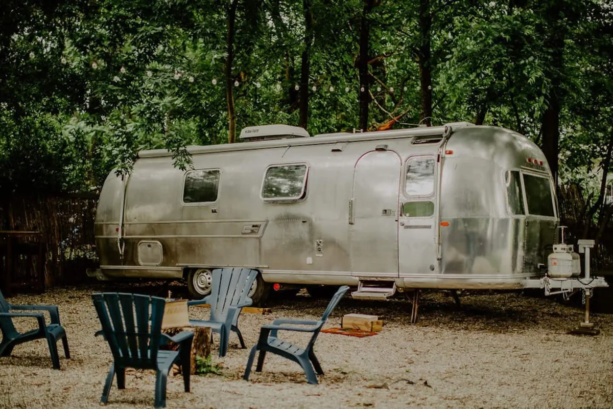 A classic Airstream trailer is nestled among natural greenery, with Adirondack chairs set up for outdoor gatherings. The scene suggests relaxation after a day of exploration, evoking glamping comfort and the retro ambiance referenced in the section.